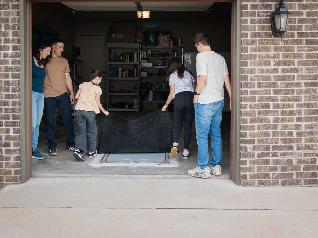 A family with small children easily lifting up the storm shelter cover. At 30lbs, the cover is heavy enough to stay put, but light enough to be pulled away quickly.